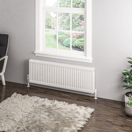 Modern white panel radiator under window in a bright room with wood floor and grey rug