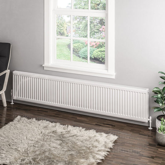Modern white horizontal radiator under window in stylish living room with grey rug