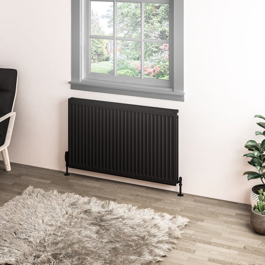 Modern black horizontal radiator under window in bright bathroom with rug and plant