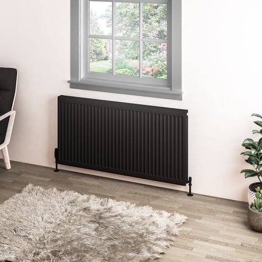 Modern black vertical radiator in a bright room with wooden floor and large window