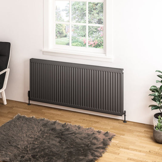 Modern grey vertical panel radiator in a bright living room with wooden flooring and large window