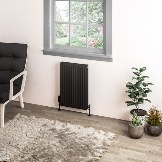 Modern black vertical radiator under window in stylish living room with plants and armchair