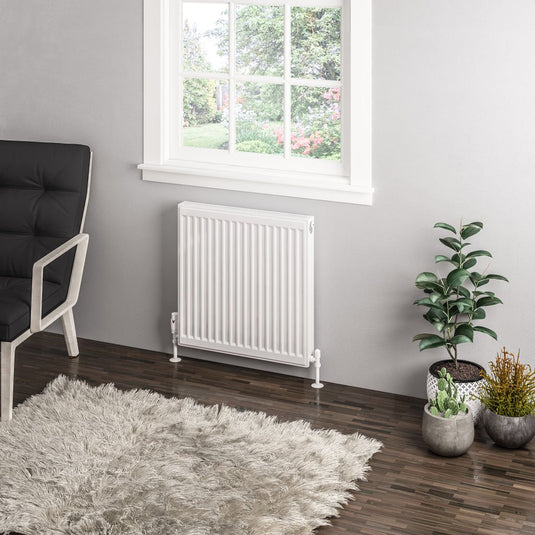 Modern white radiator under window in living room with wood floor, rug, and potted plants