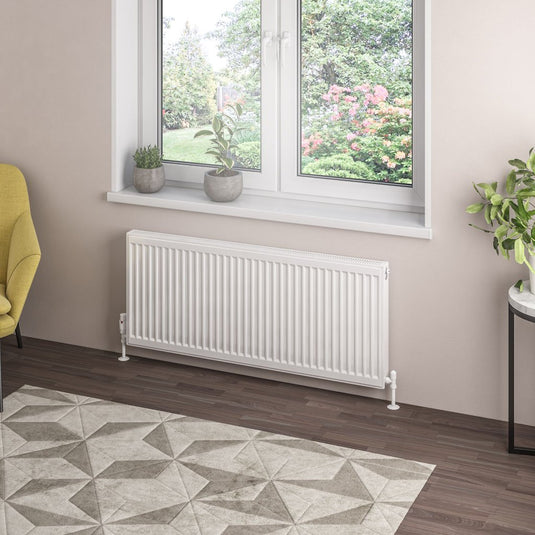Modern white panel radiator under window, indoor plants, hardwood floor, geometric rug