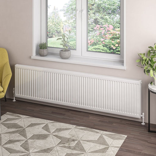 Modern white horizontal radiator beneath window in bright home interior with indoor plants