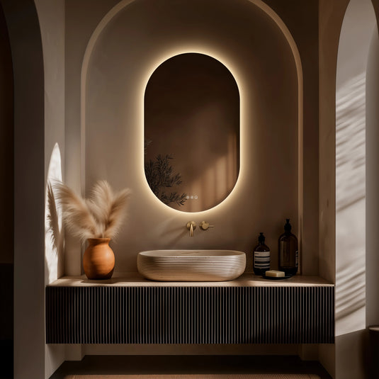 Oval bathroom mirror with LED lighting above modern vanity, decorative vase, and soap dispenser