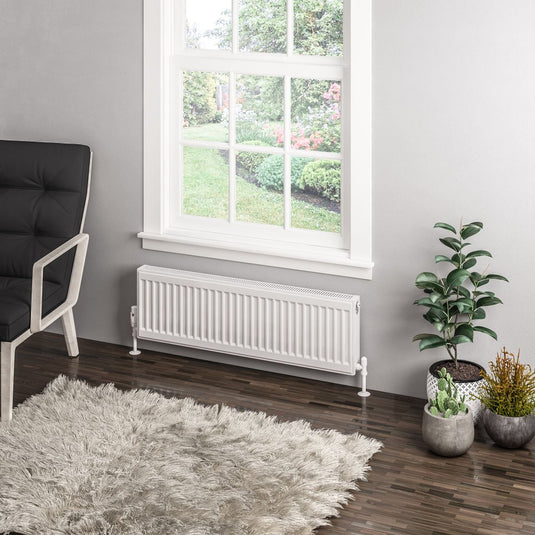 Modern white panel radiator under window in bright living room with indoor plants and rug