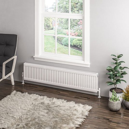 Modern white panel radiator under window in cozy living room with indoor plants and rug