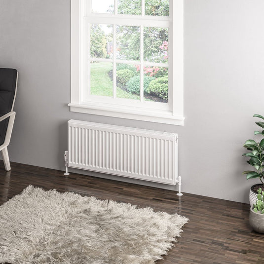 Modern white panel radiator under window in minimalist living room with grey rug and plants