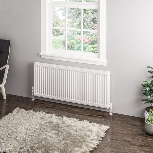 Modern white double panel radiator under window in stylish living room with rug and plant