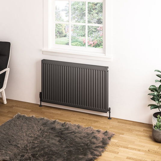 Modern dark grey radiator under window in bright bathroom with plant and fluffy rug