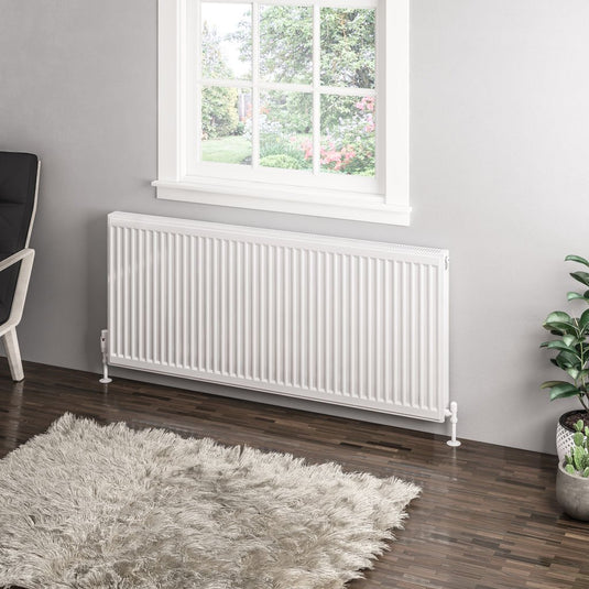 Modern white horizontal radiator below window in stylish living room with rug and houseplant
