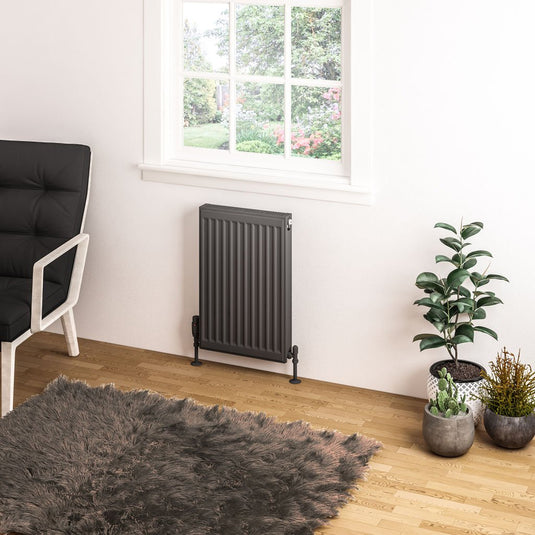 Modern vertical radiator under window in a cozy living room with indoor plants and armchair