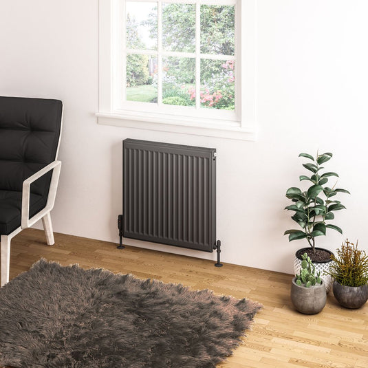 Modern black panel radiator under window in cozy living room with plants and grey rug