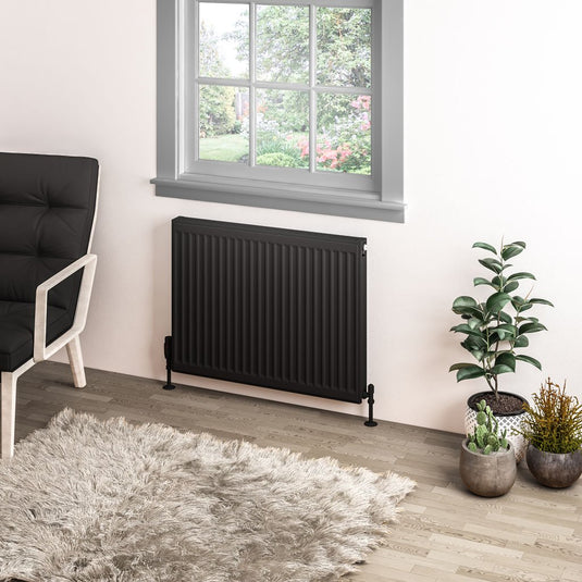 Modern black vertical radiator under window in stylish living room with plants and armchair