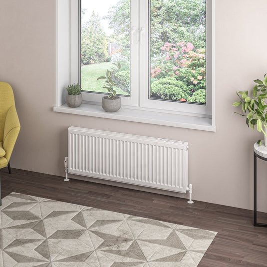 Modern white panel radiator under window in bright living room with indoor plants