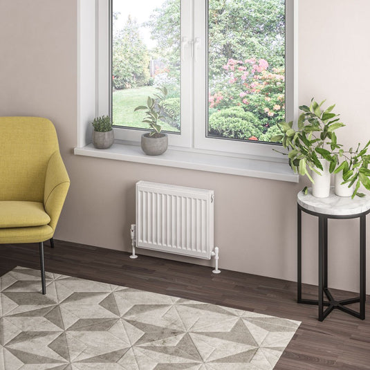 Modern radiator under window in light, contemporary room with plants and yellow chair