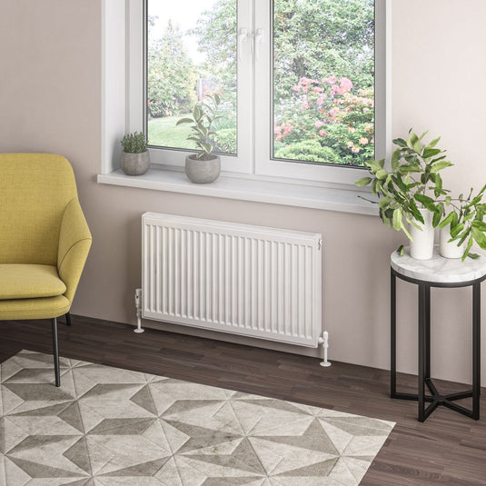Modern white panel radiator under window in stylish living room with plants and geometric rug