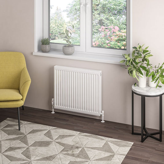 Modern white panel radiator under window in bright living room with yellow chair, plants, and geometric rug
